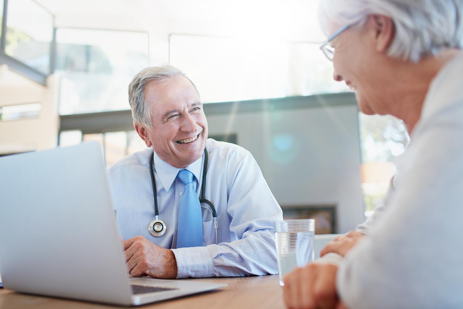 Kedves idősebb doktor kikérdezi a páciens és rögzíti az orvosi szoftverbe az információkat.